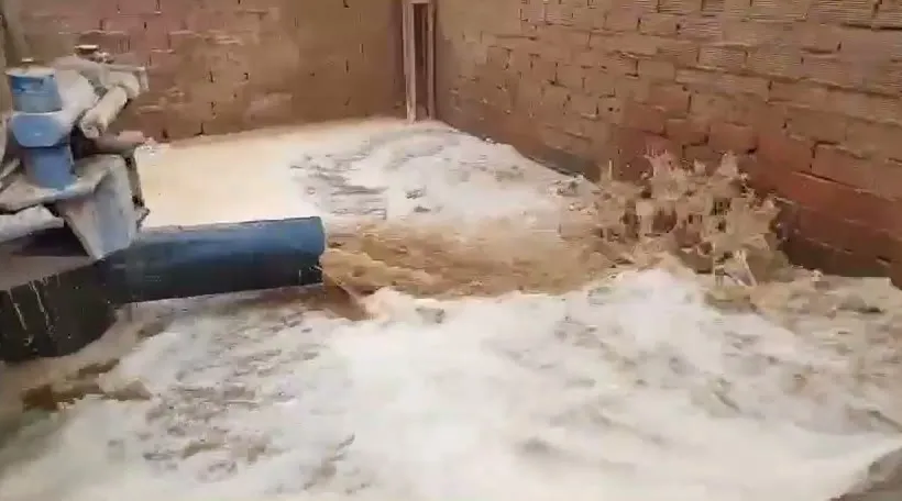 Agua saliendo con fuerza por la tubería de una máquina de sondeo, junto a un muro de ladrillo