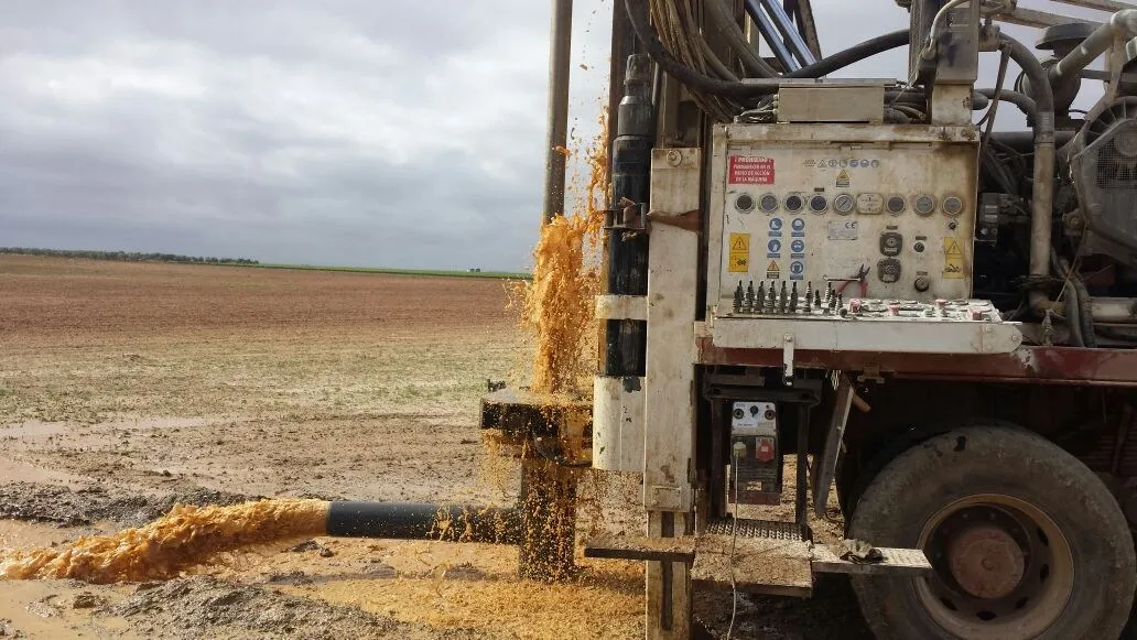 Máquina de sondeo perforando en una finca de Extremadura, con el agua saliendo del pozo