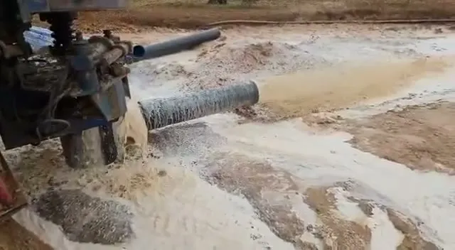 Detalle de la máquina de sondeo con el tubo vertiendo agua en la finca